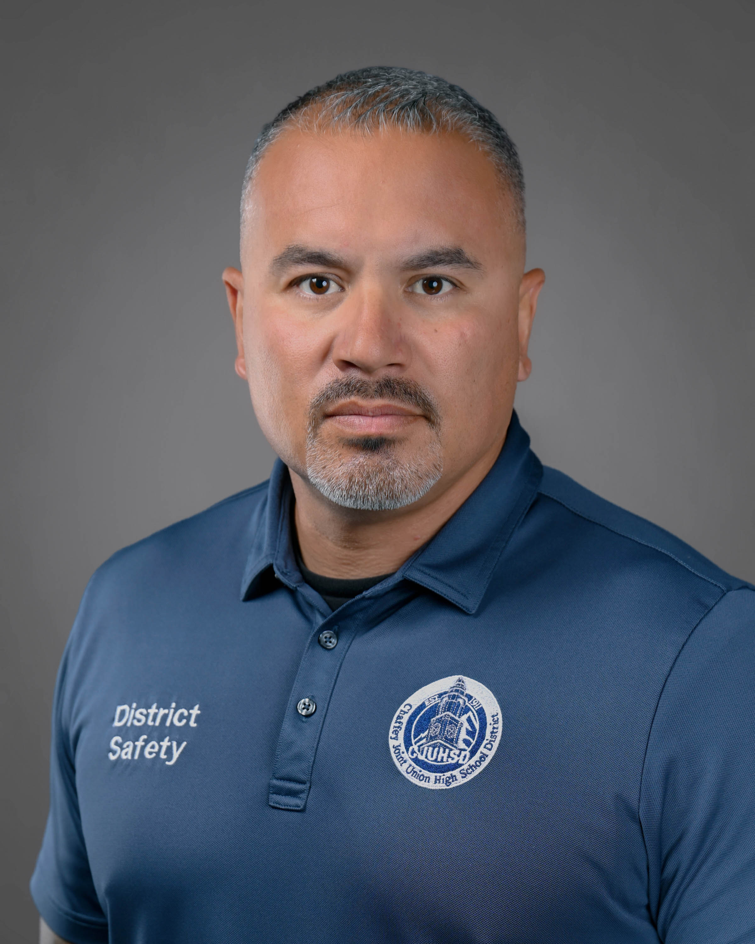 Serious man with a high fade haircut and goatee wearing a blue polo shirt.